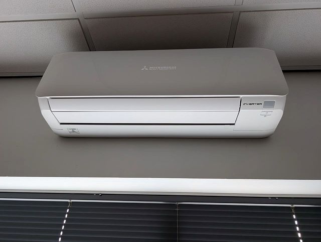 Witte airco-unit aan de wand boven een raam met lamellen.