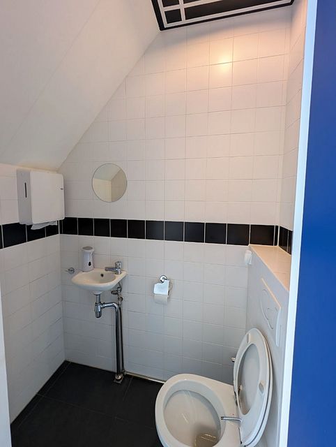 Toilet met witte wandtegels en een zwarte tegelrand, een fonteintje met een ronde spiegel erboven.